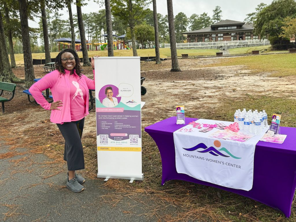 Dr. Amber Glenn standing in front of a table with a purple tablecloth at a Walk with a Doc event.